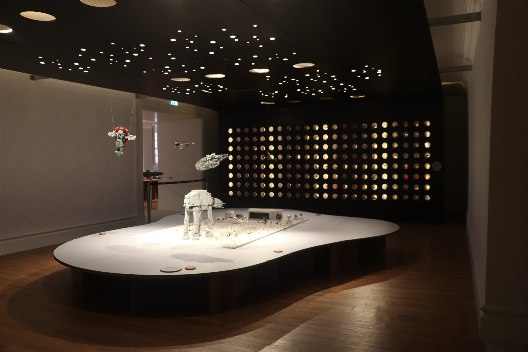 The dark room seen wide, with builds suspended over a white island