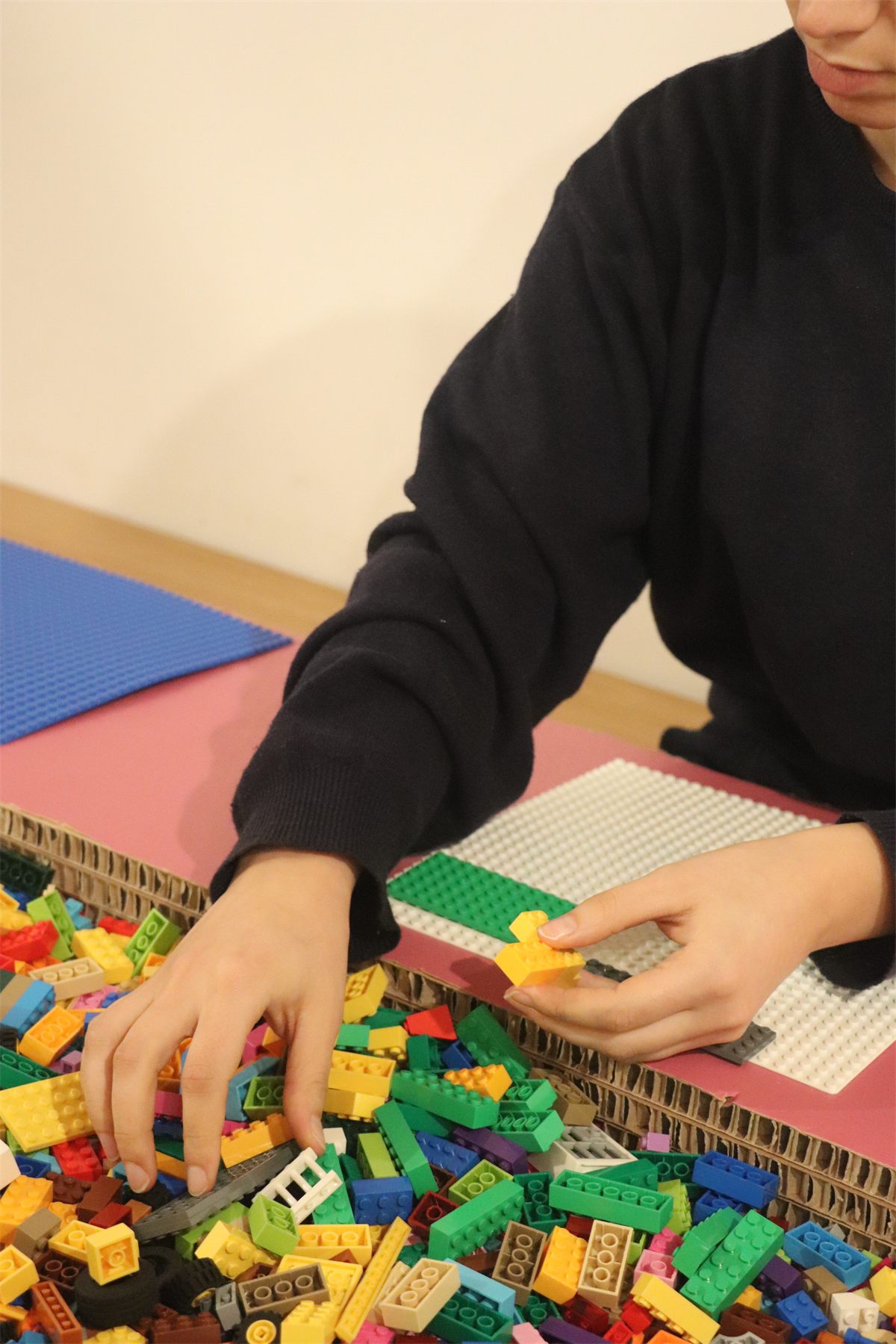 Hands assembling a LEGO build from a tray of loose bricks