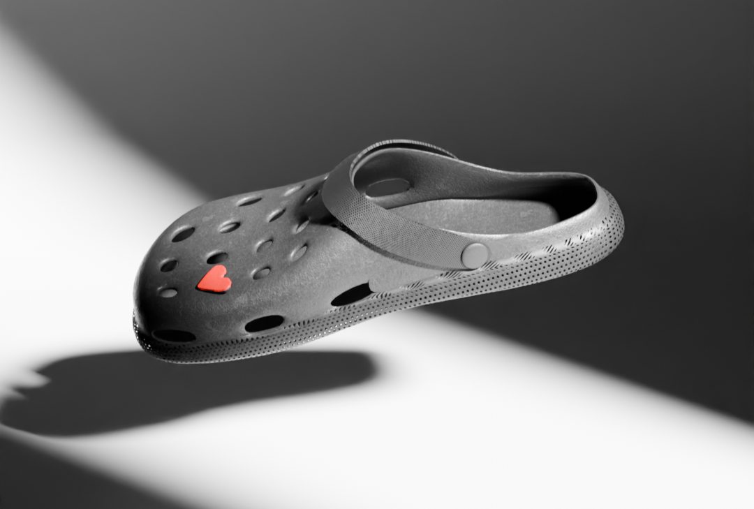 A black Croc with a red heart charm, lit against white
