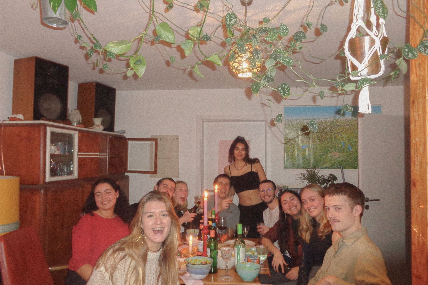 A long table of friends at dinner in a room full of plants