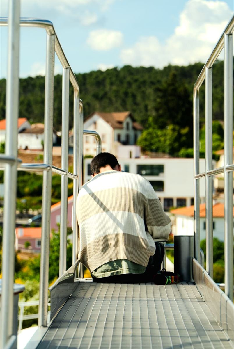 Drawing on a metal walkway above a village, seen from behind in the afternoon sun