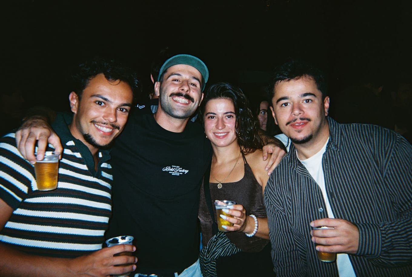 Four friends with beers, arms around each other, at a party at night