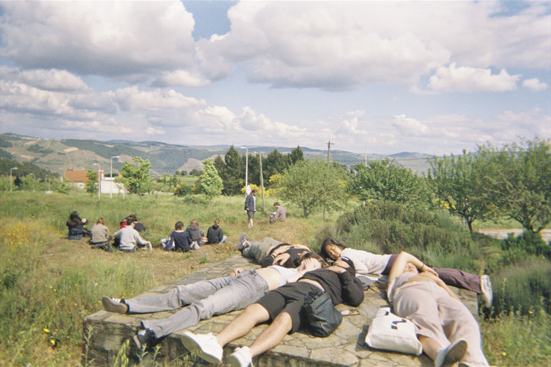 A group lying along a low wall in open country, hills and cloud behind them