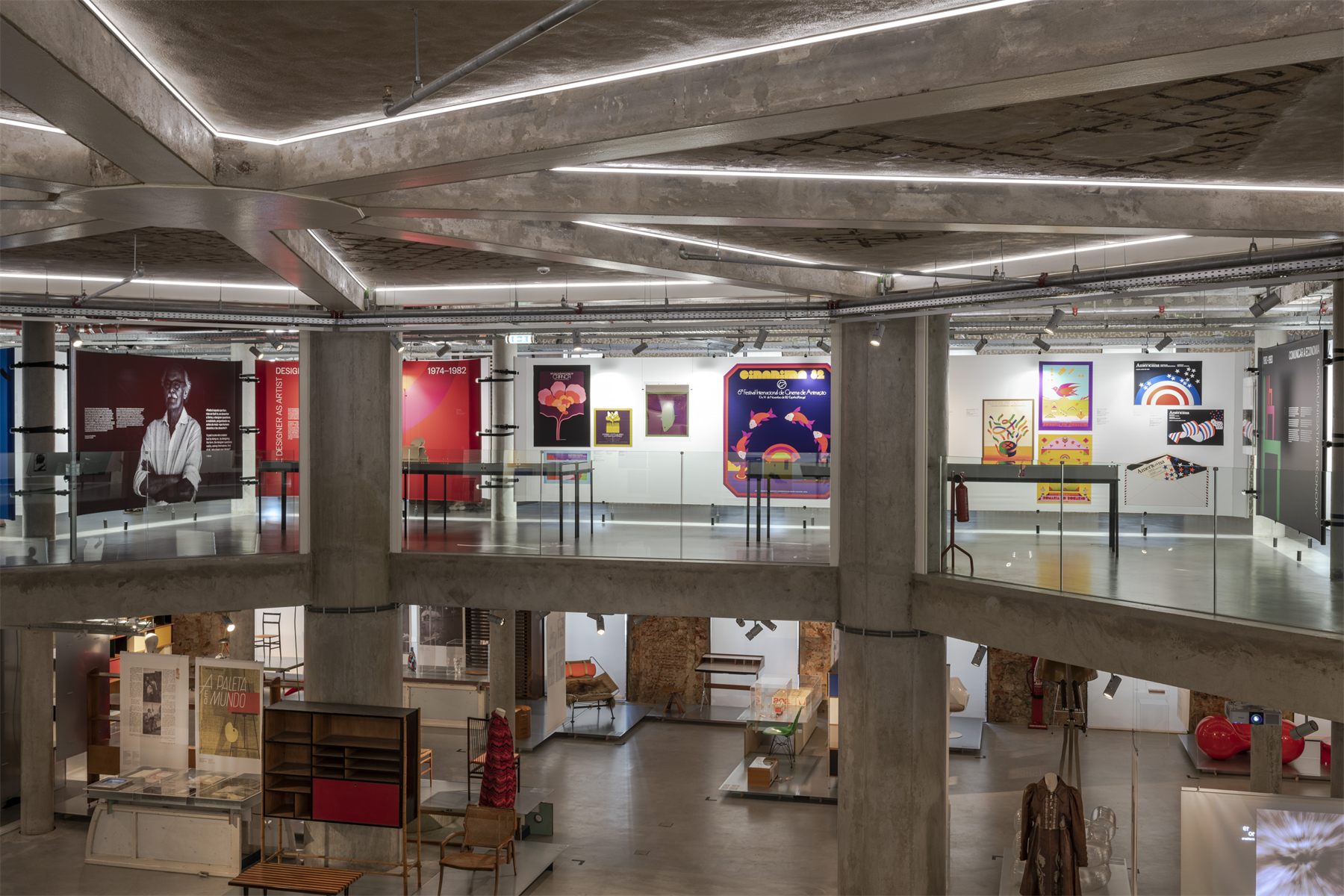 The double-height hall at MUDE, with concrete columns and exposed services above the exhibition