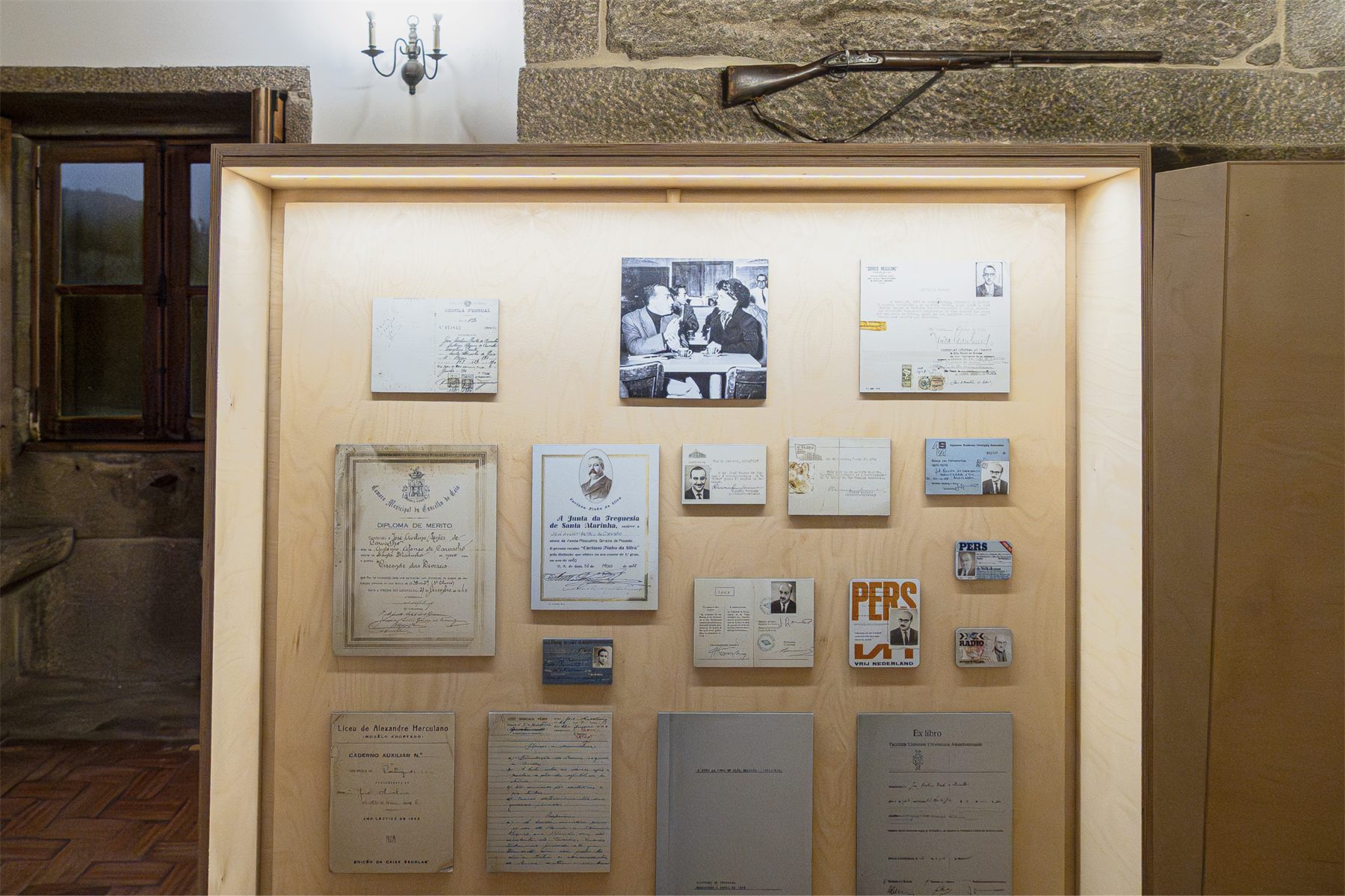A lit vitrine holding framed documents against a plywood ground