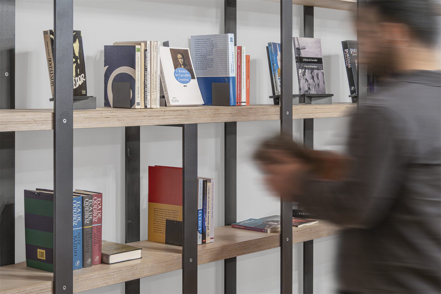 Espaço José Rentes de Carvalho: the writer’s books on the plywood and steel shelving, a visitor passing