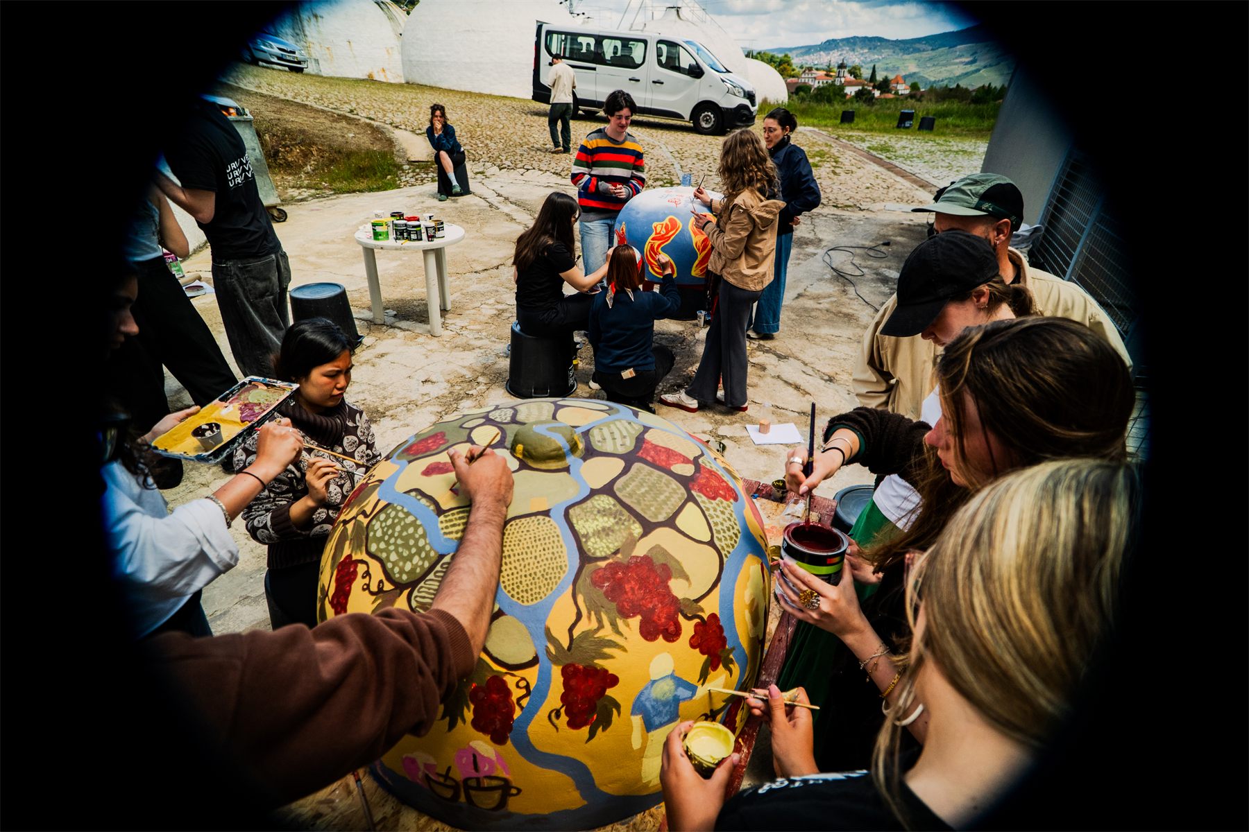 Seen from above: a group crowded around a painted model tank, brushes and paint pots everywhere