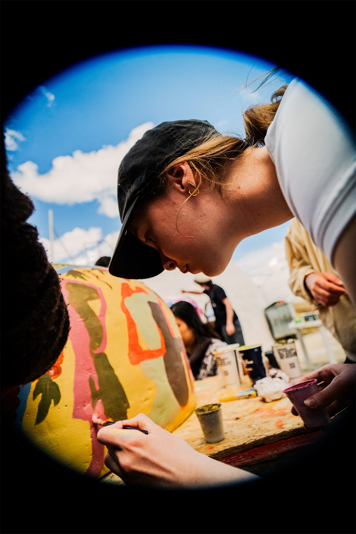 A participant leaning over a scale model of a wine tank, painting it, blue sky above