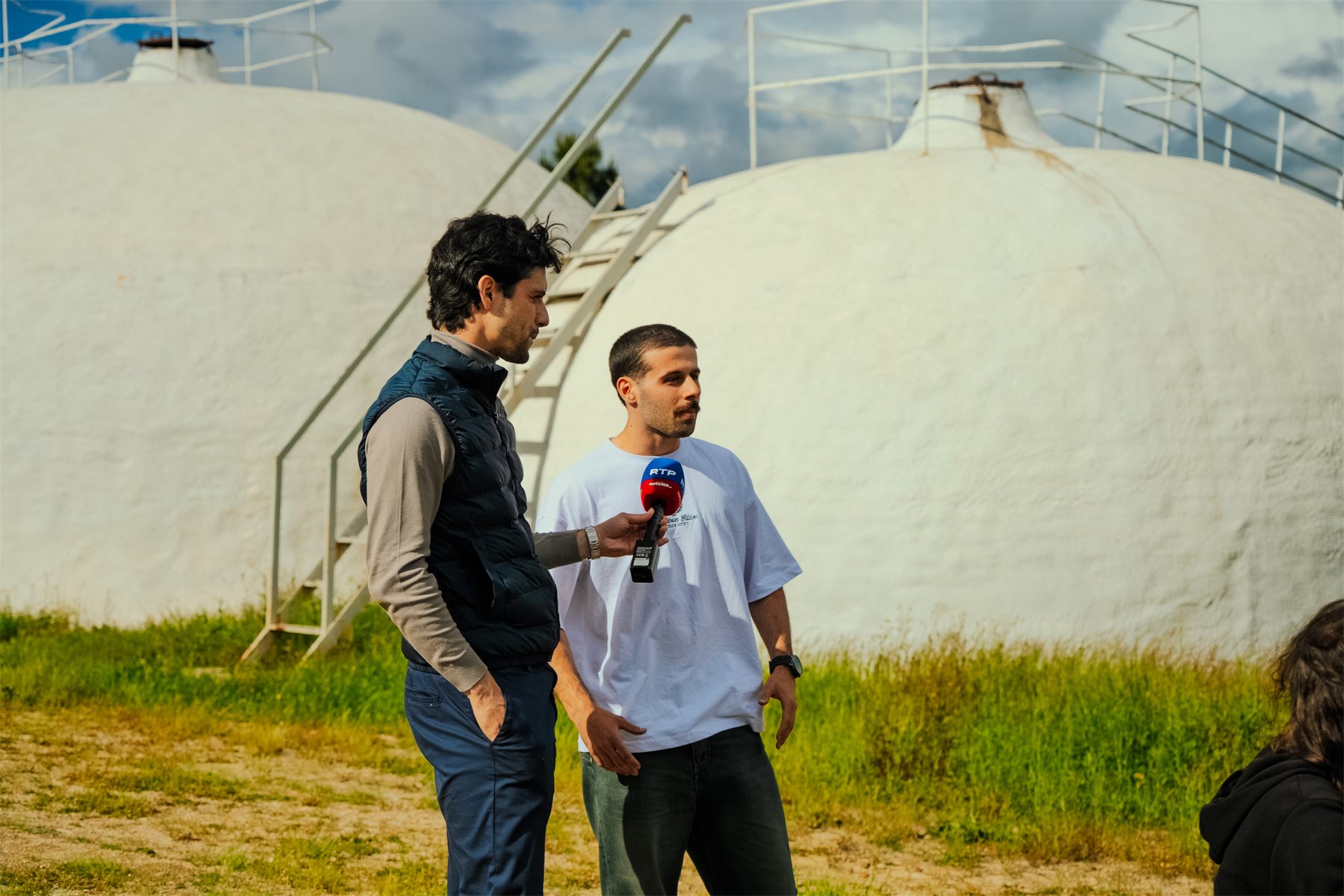 An RTP reporter interviewing one of the organisers in front of the adega&rsquo;s white domed tanks