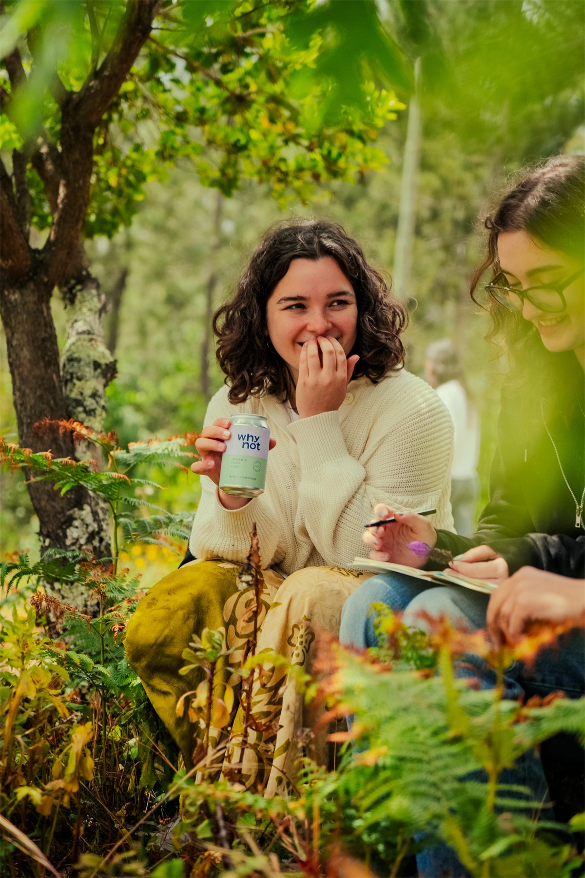 Two participants sitting among the ferns, laughing, drinks in hand