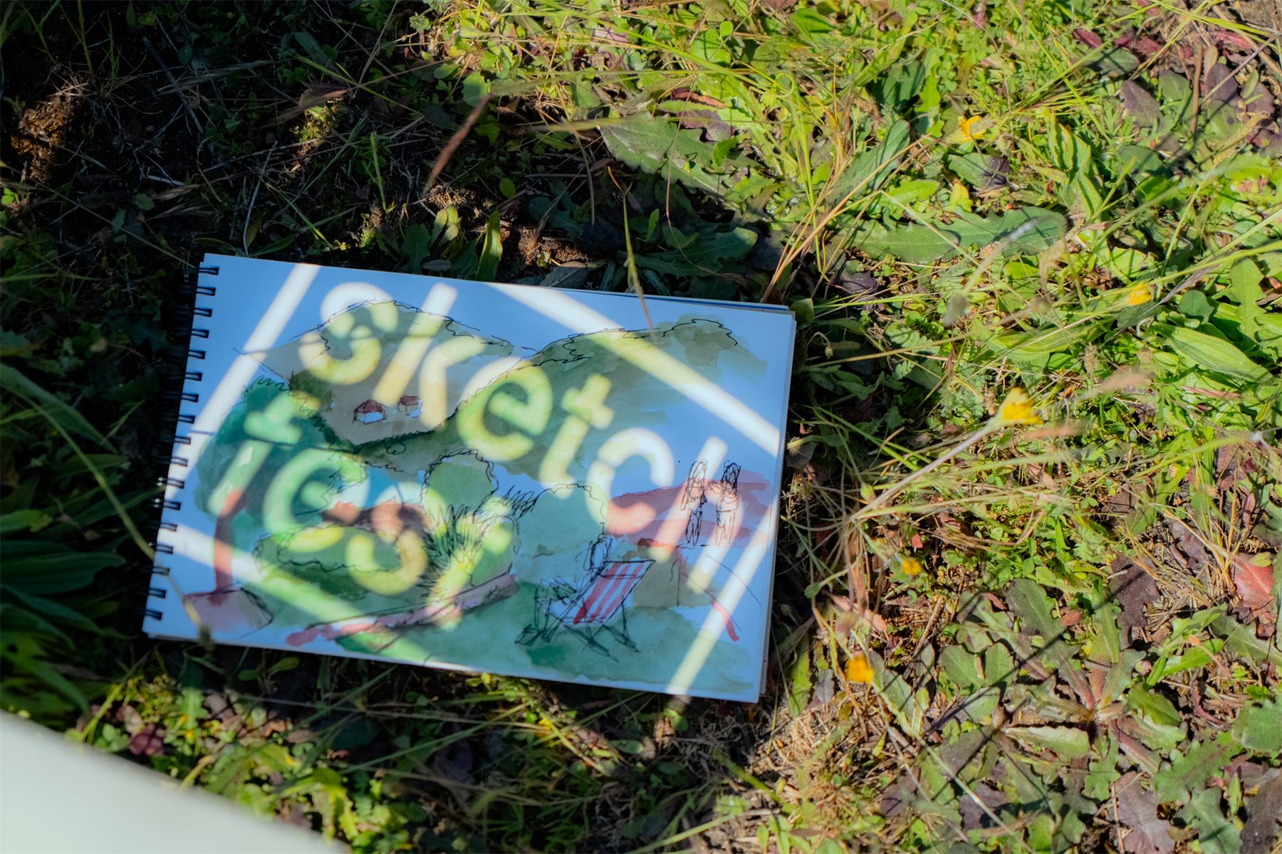 A sketchbook open in the grass, a watercolour of the valley on the page